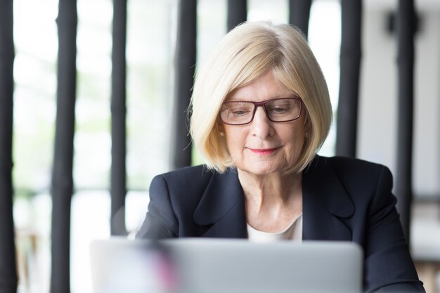 Positieve senior zakenvrouw die op laptop werkt