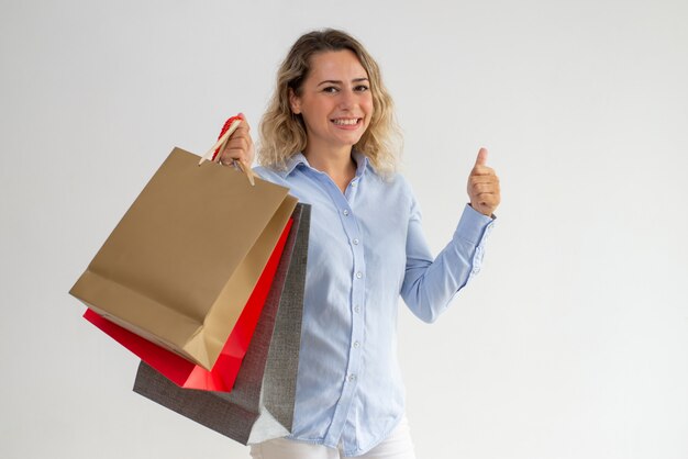 Positieve vrouw boodschappentassen houden en tonen duim omhoog