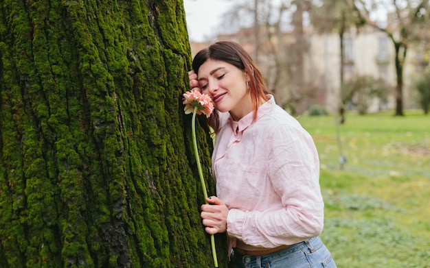 Positieve vrouw met bloem dichtbij boom in park