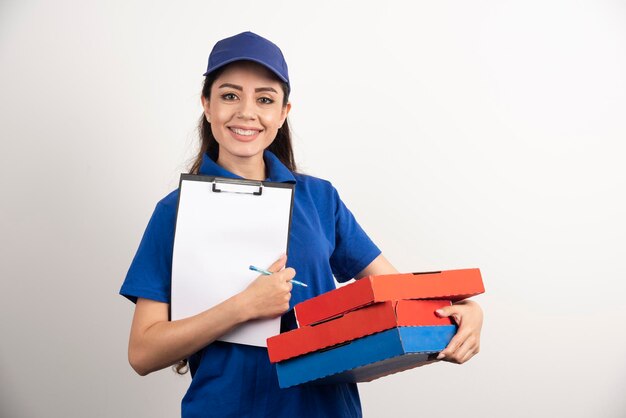 Positieve vrouwelijke koerier met karton van pizza en klembord