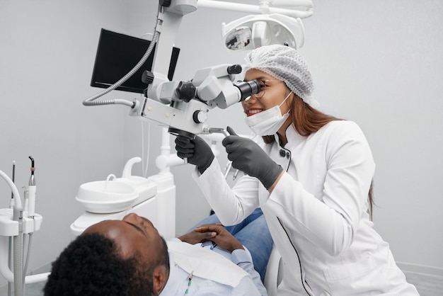 Positieve vrouwelijke tandarts die tanden van mannelijke patiënt geneest