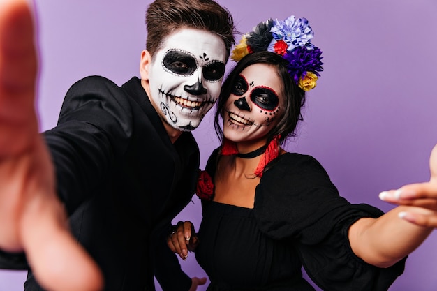 Positieve zombie man selfie maken in studio met vriendin. Gelukkige vrienden in maskeradekostuums die pret hebben.