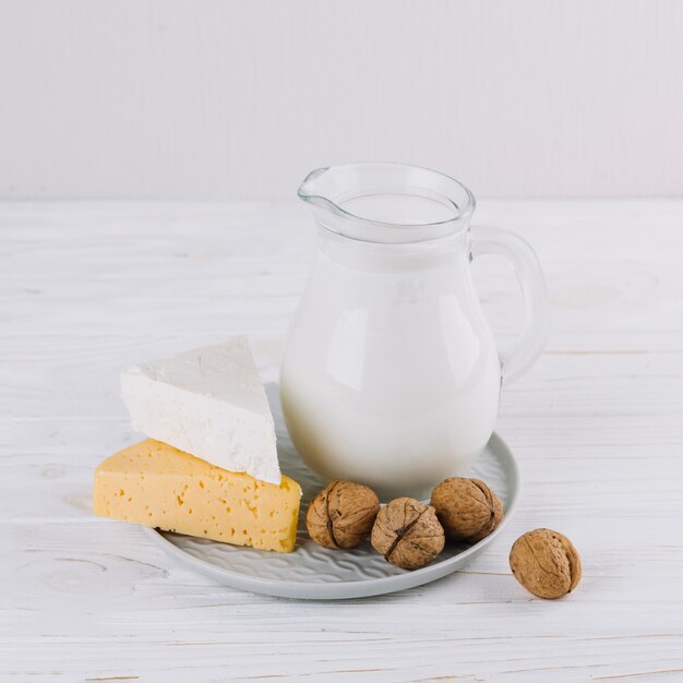 Pot met melk; kaas en walnoten op witte houten tafel