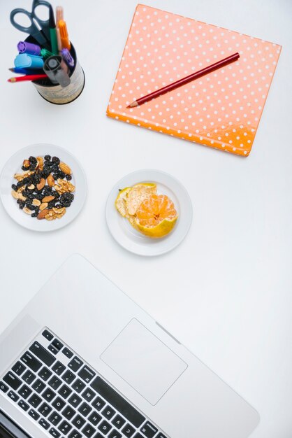 Potlood; notebook; noten eten; laptop en oranje op wit oppervlak