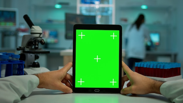 Pov shot van scheikundige met behulp van tablet met groen scherm in biologisch laboratorium. medisch werker met een witte jas in een kliniek die werkt met een notebook met chromakey op een geïsoleerd scherm in een medisch laboratorium