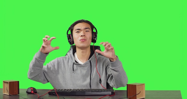 Gratis foto pov van een man die online spelletjes speelt op een pc terwijl hij met zijn vrienden speelt met koptelefoon op zijn bureau aziatische gamer die plezier heeft met een actiespel op een werkstation met een groen scherm op de achtergrond