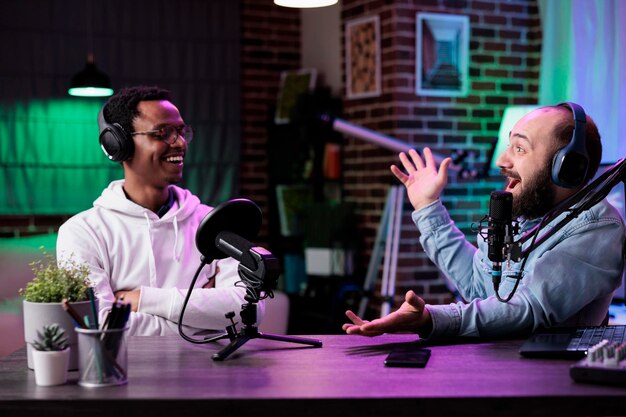 POV van mannelijke bloggers die vloggen met podcastgesprekken op camera, met behulp van streamingapparatuur in studio met neonlichten. Contentmakers die plezier hebben met het filmen van online afleveringen voor sociale media.