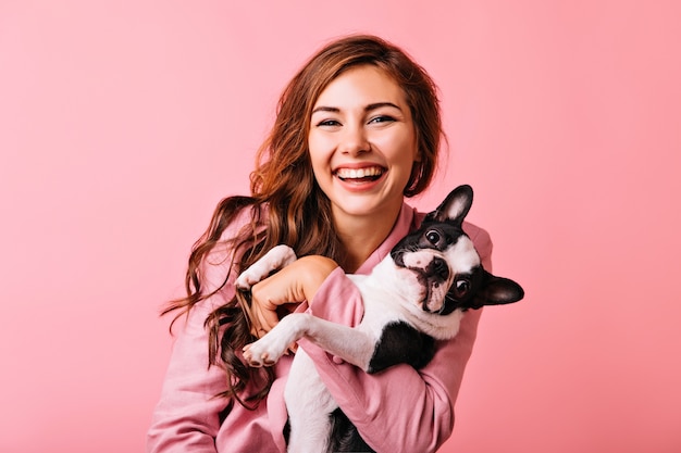 Prachtig Europees vrouwelijk model chillen met puppy. Indoor portret van debonair meisje genieten van portretshoot met haar schattige huisdier.