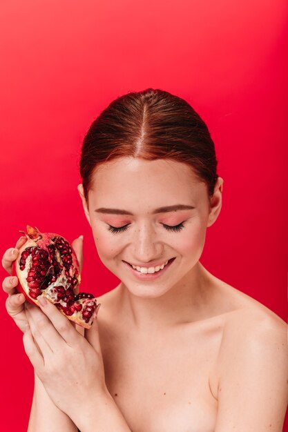 Prachtig gember meisje met granaat lachen met gesloten ogen. Studio shot van zalige jonge vrouw poseren met rijpe granaatappel.