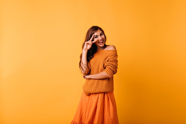 Gratis foto prachtig kaukasisch meisje in trendy oranje trui glimlachen. indoor portret van prachtige jonge vrouw draagt lichte kleding.