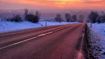 Gratis foto prachtig landschap van een weg omgeven door bomen bedekt met sneeuw bij zonsopgang