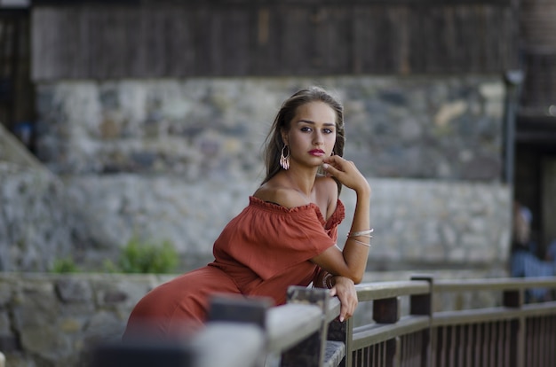 Gratis foto prachtig shot van een vrouwelijk model in een roodoranje jurk op een balkon met een wazige stad