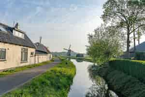 Gratis foto prachtig shot van een waterkanaal langs een smal weggetje met een windmolen op een veld