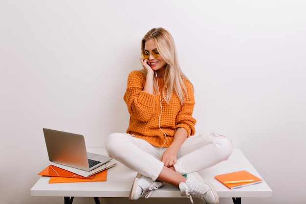 Prachtig vrouwelijk model in casual kleding ontspannen aan de tafel met een glimlach en kijken naar laptop scherm