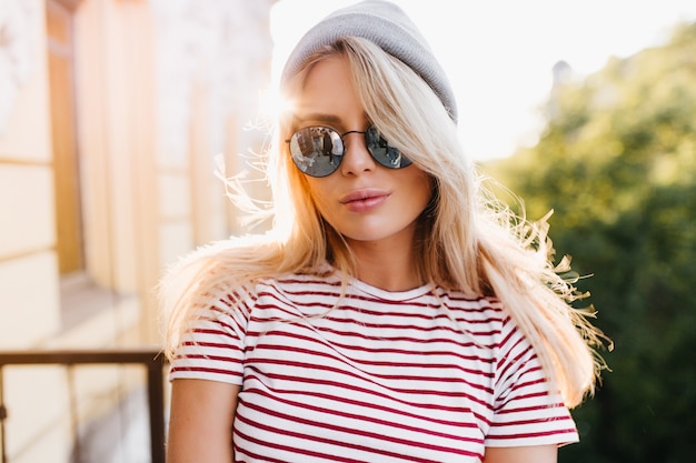 Prachtige blonde vrouw in zomerkleding poseren op balkon vroeg in de avond genieten van zonlicht