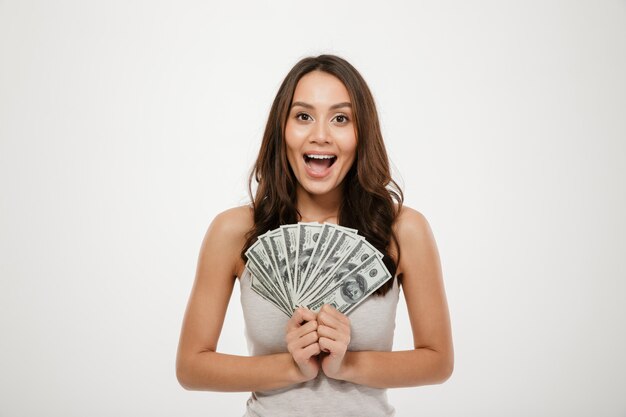 prachtige brunette vrouwelijk model met lange haren die fan van 100 dollarbiljetten, rijk en gelukkig over witte muur