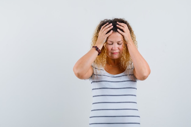 Prachtige dame die handen op het hoofd houdt in gestreept t-shirt en er depressief uitziet, vooraanzicht.