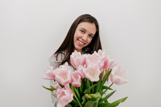 Prachtige gelukkige vrouw met donker haar en mooie gelukkige glimlach poseren voor de camera met tedere roze bloemen over geïsoleerde achtergrond gelukkige vrouw viert womans day