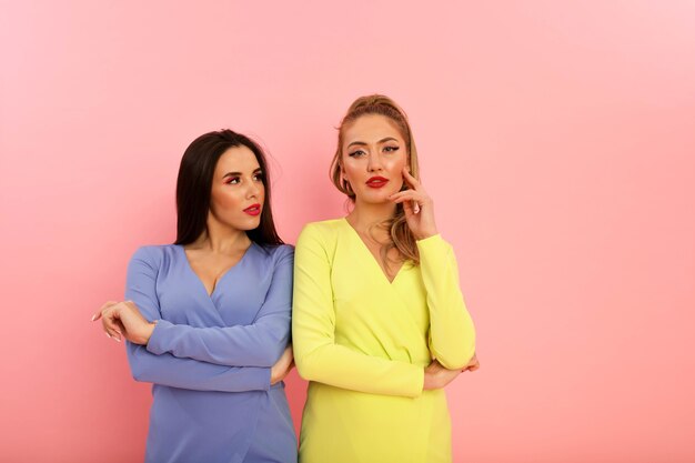 Prachtige heldere dames in stijlvolle zomerjurken, geel en blauw. Blond en brunette met grote rode lippen en modern kapsel. Welgevormde hete lichamen, sexy modellen. Schieten in de studio op de achtergrond van de pin