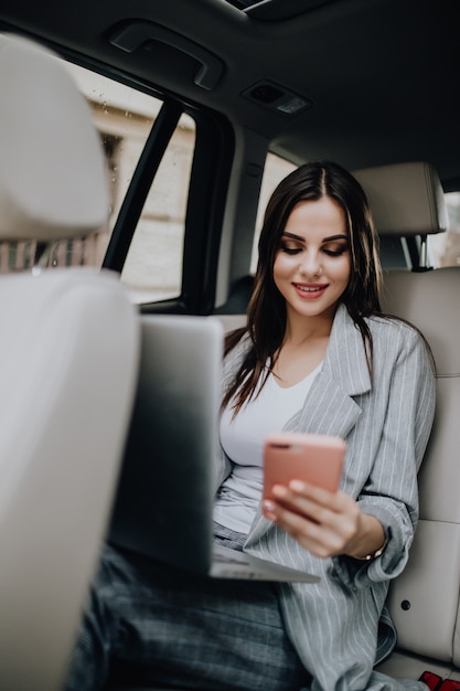 Prachtige jonge vrouw met laptop in de auto zitten en praten over de telefoon