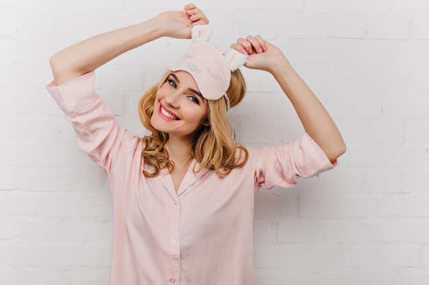 Prachtige jonge vrouw met trendy kapsel die zich uitstrekt in de ochtend. Leuk meisje in roze eyemask positieve emoties uitdrukken.