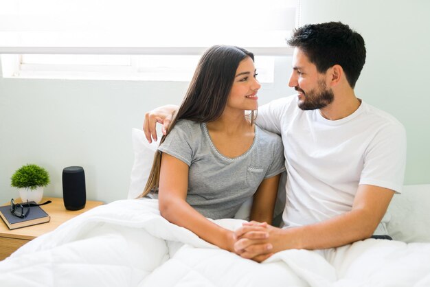 Prachtige jonge vrouw wakker in bed met haar knappe vriendje. Aantrekkelijk stel in pyjama dat elkaar in de ogen kijkt en verliefd is