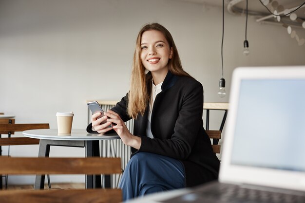 Prachtige jonge vrouwelijke student zitten in café en het gebruik van smartphone