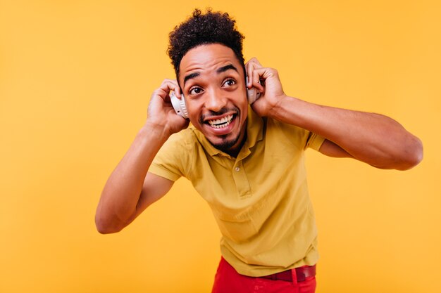 Prachtige man met grote donkere ogen muziek luisteren. Binnenfoto van vrolijk Afrikaans mannelijk model in witte hoofdtelefoons.