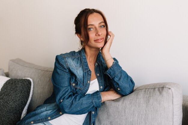 Prachtige vrouw in denim overhemd poseren op een witte achtergrond thuis