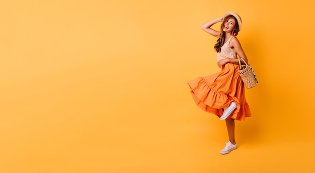 Gratis foto prachtige vrouw in lange lichte rok dansen in de studio. zorgeloos geïnspireerd vrouwelijk model poseren met plezier op geel.