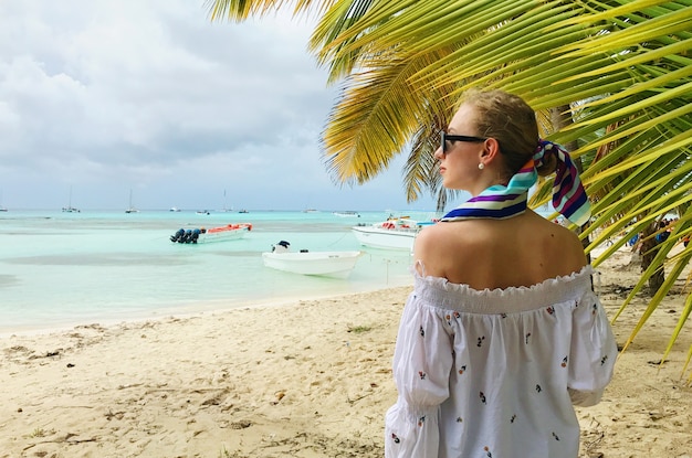 Gratis foto prachtige vrouw in wit shirt staat onder de palm