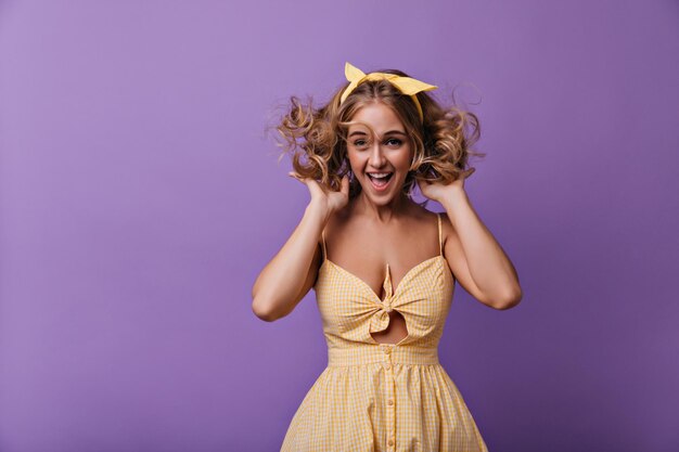 Prachtige vrouw met bronzen huid die op paarse achtergrond springt Binnenfoto van schattig lachend meisje met blond krullend haar