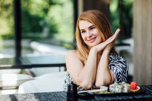 Prachtige vrouw van middelbare leeftijd zit op caféterras met een bord sushibroodjes