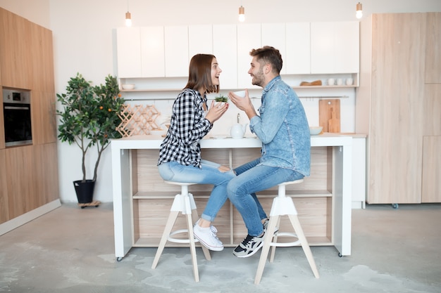 Pratende jonge gelukkig man en vrouw in keuken, ontbijt, paar samen in de ochtend, glimlachen, met thee