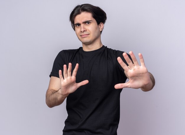 Preek jonge knappe kerel die zwarte t-shirt draagt die stopgebaar toont dat op witte muur wordt geïsoleerd