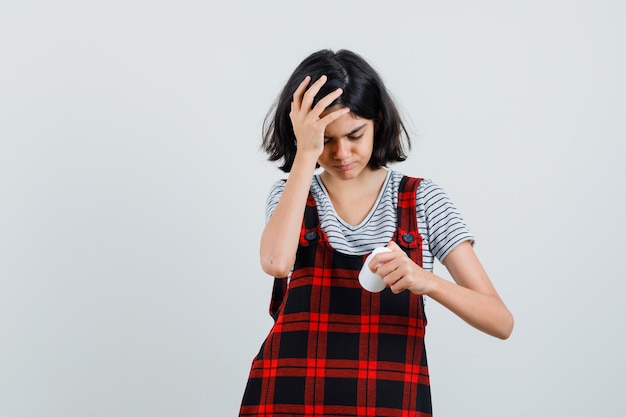 Preteen meisje hoofdpijn tijdens het kijken naar fles pillen in t-shirt, jumpsuit, vooraanzicht.