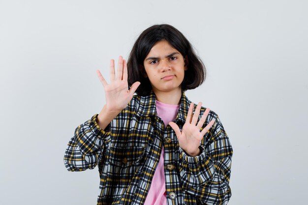 Preteen meisje in shirt, jas die handen opsteekt om te verdedigen en er ontevreden uit te zien, vooraanzicht.