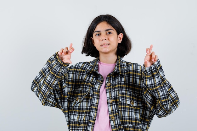 Preteen meisje in shirt, jas met haar gekruiste vingers, vooraanzicht.