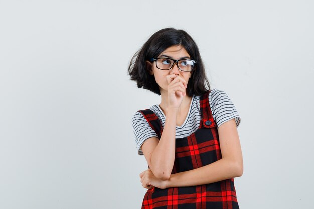 Preteen meisje in t-shirt, jumpsuit, bril denken en peinzend kijken