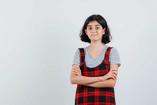 Preteen meisje permanent met gekruiste armen in t-shirt, jumpsuit en op zoek tevreden. vooraanzicht.