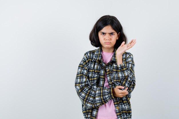 Preteen meisje spreidt open palm opzij in shirt, jas en ziet er ontevreden uit. vooraanzicht.