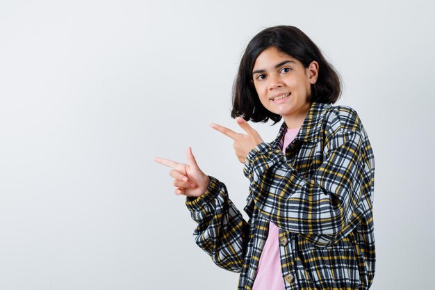 Preteen meisje wijst opzij in shirt, jas en ziet er blij uit, vooraanzicht.