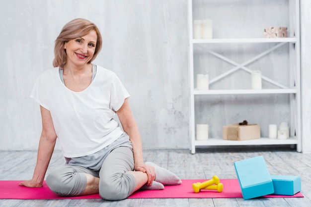 Pretty lachende vrouw zitten in de buurt van blokken en halters op yoga mat