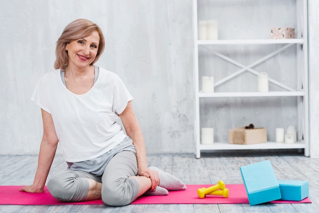 Gratis foto pretty lachende vrouw zitten in de buurt van blokken en halters op yoga mat