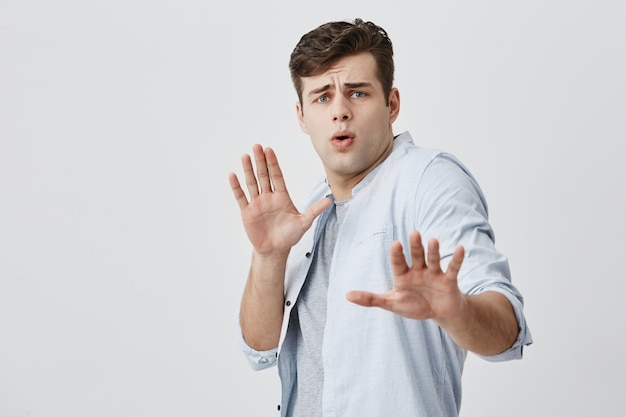 Preutse Kaukasische knappe kerel met donker haar die eindeteken met palmen tonen terwijl zijn meisje hem van iets probeert te beschuldigen. Bange jongeman riep en fronste zijn gezicht