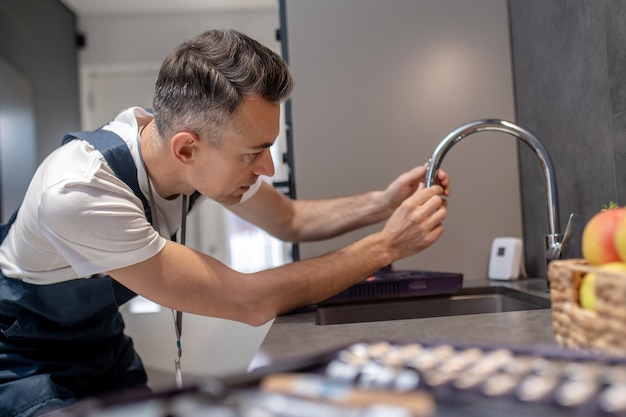 Preventie van waterkraan Geconcentreerde man die over de waterkraan leunt en de uitlooppijp aanraakt