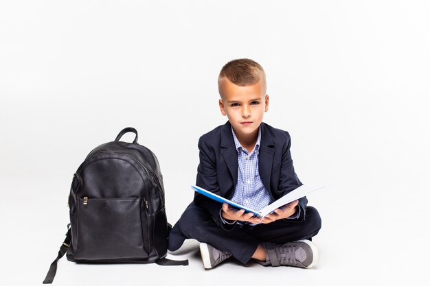 Primaire schooljongenzitting op vloer en lezing geïsoleerd op witte muur