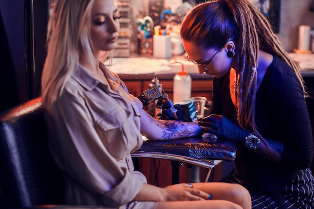 Proces van het creëren van nieuwe tatoeage voor jonge vrouw door ervaren tatoeëerder in studio.
