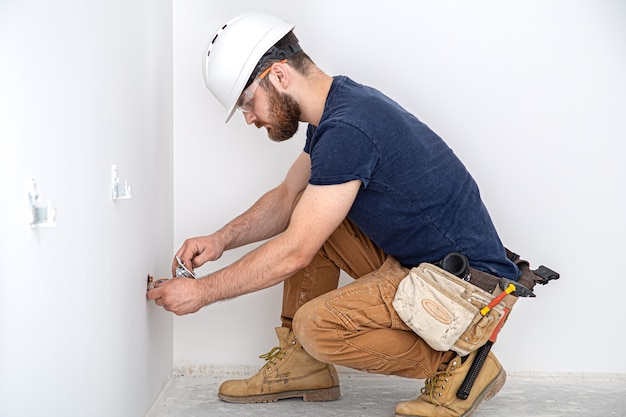 Professioneel in overall met een elektriciensgereedschap op de witte muurachtergrond. Huisreparatie en elektrisch installatieconcept.