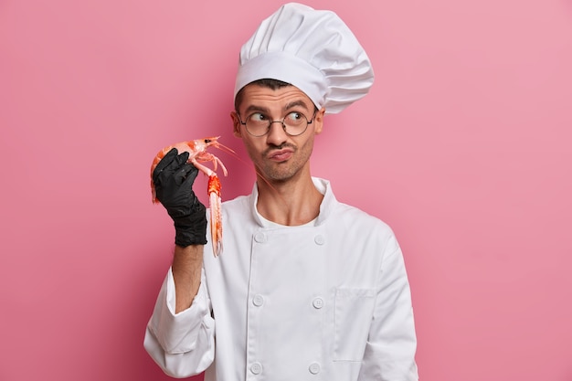 Professionele chef-kok kookt zeevruchten, gezond vegetarisch eten, houdt rivierkreeftjes vast, draagt een wit kokuniform